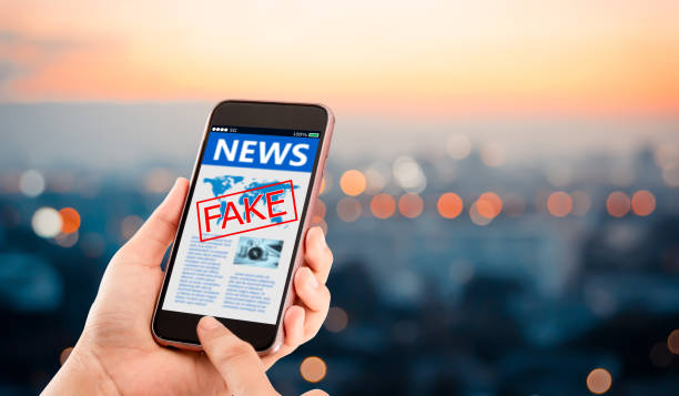 Hands holding mobile phone with fake news message on a blurred night city as background
